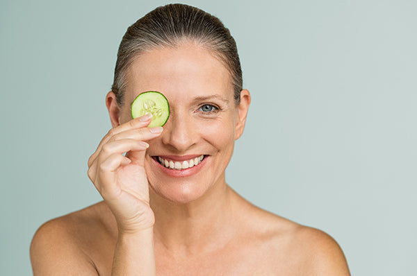 Image of mature woman holding a cucumber slice over her eye