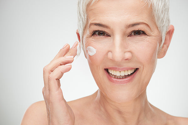 Image of laughing mature woman applying moisturiser for mature skin