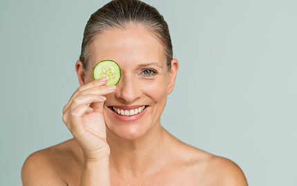 Image of mature woman holding a cucumber slice over her eye