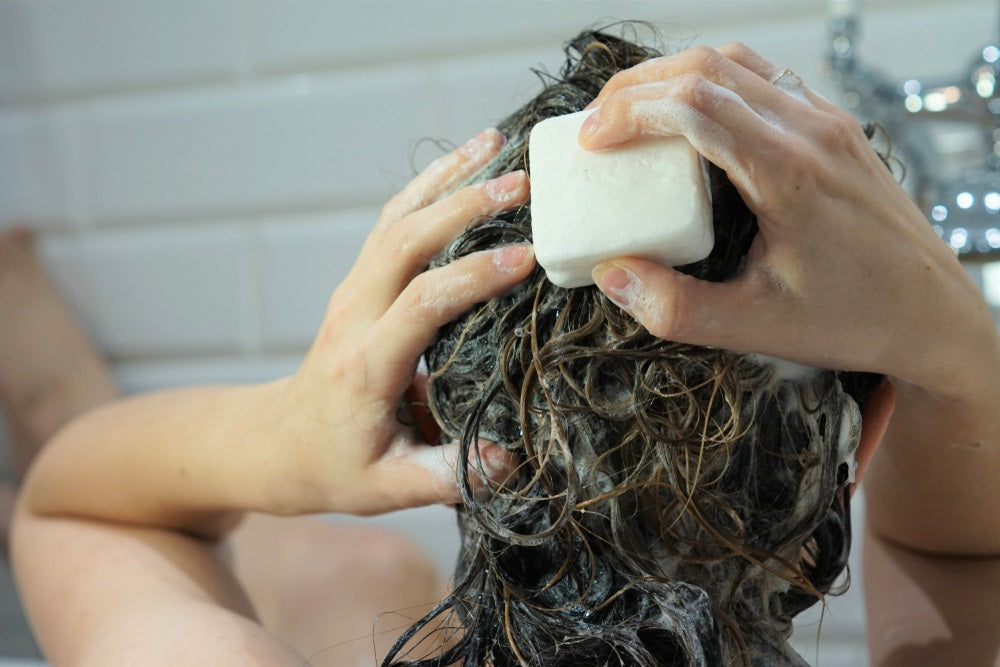 Woman washes her brown hair with homemade shampoo bar or soap, zero waste concept.